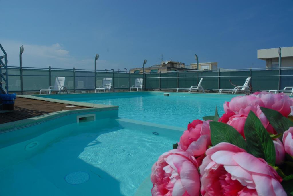uma piscina com flores rosas no primeiro plano em Residence Hotel Club House em Cattolica