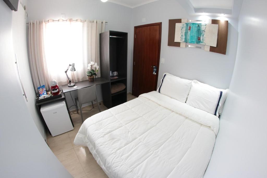 a bedroom with a white bed and a desk at Santo Antônio Hotel Ltda in Angatuba