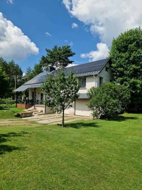 a white house with a tree in the yard at Vila Varėna in Varėna