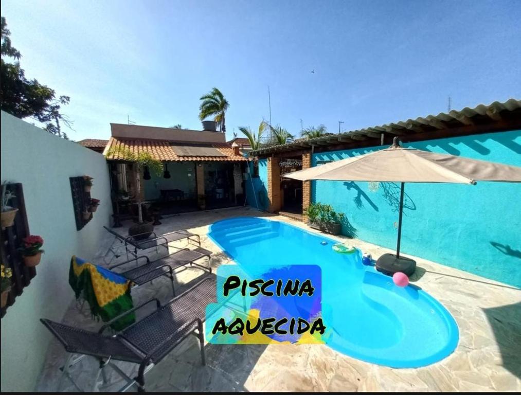 a swimming pool with an umbrella next to a house at Pousada Flores em Vida in Olímpia