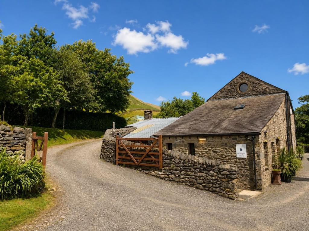 a stone building with a fence and a road at Howgills Barn in Sedbergh