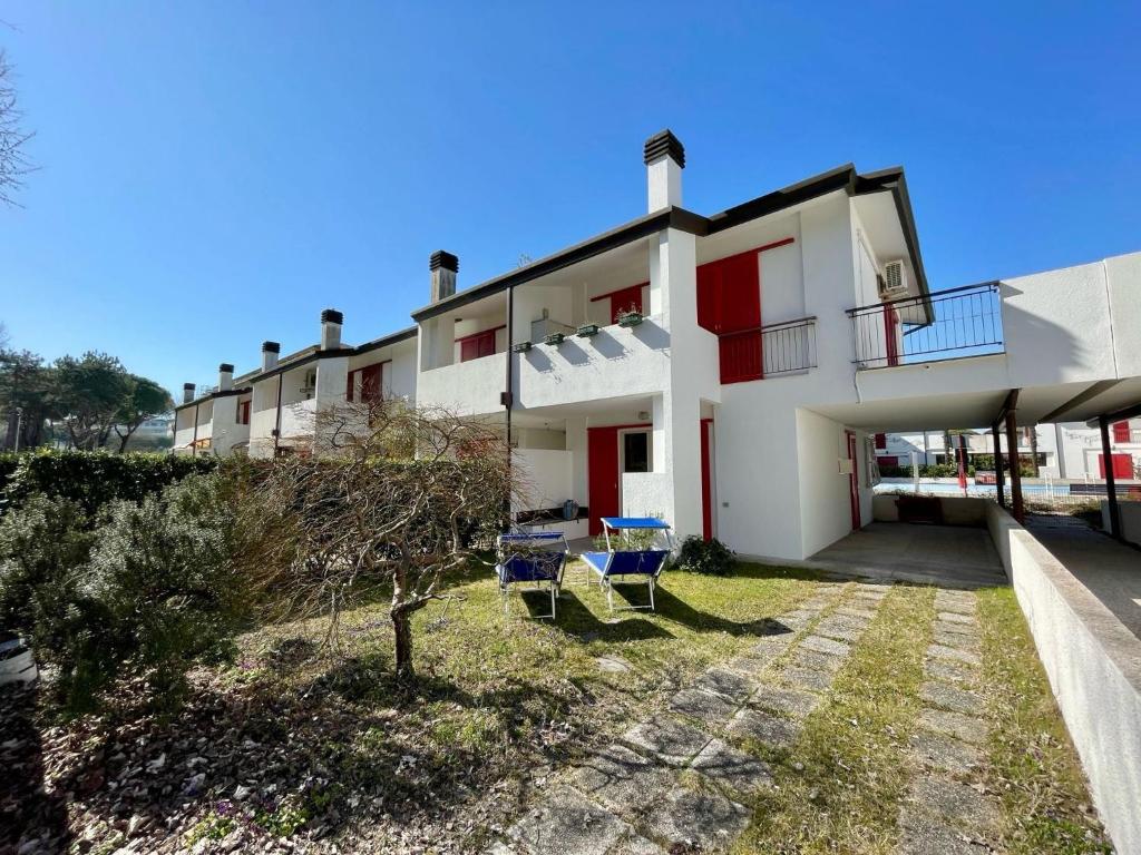 a large white house with two chairs in the yard at Terraced house with garden and pool in Porto Santa Margherita di Caorle