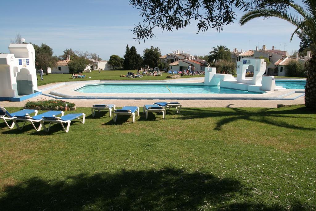 a swimming pool with lounge chairs in the grass at Pedras Del Rei Holiday House in Tavira