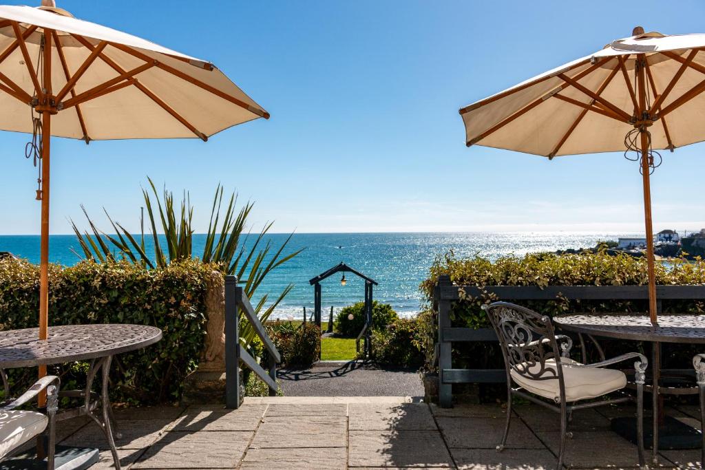 a patio with tables and umbrellas and the ocean at The Bay Hotel in Coverack