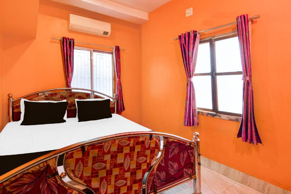 a bedroom with a bed with orange walls and windows at Capital O Sri Krishna Palace Near Sum Hospital in Durgāpur