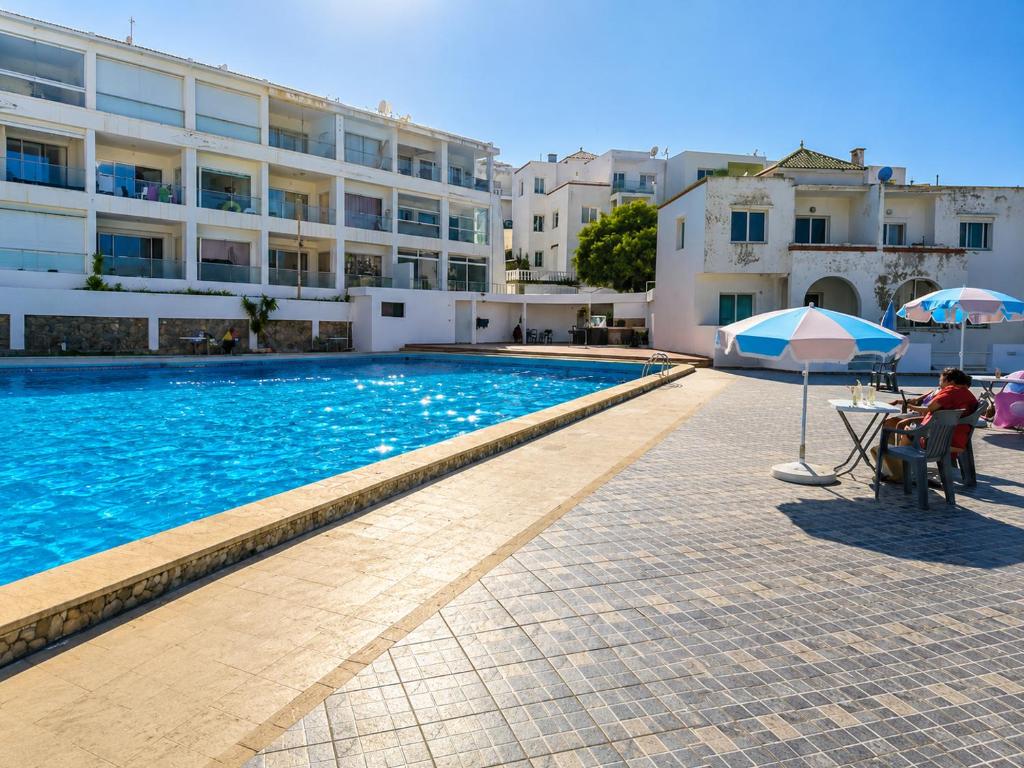 a swimming pool with a table and an umbrella next to a building at Résidence Tarifa in Mrarech