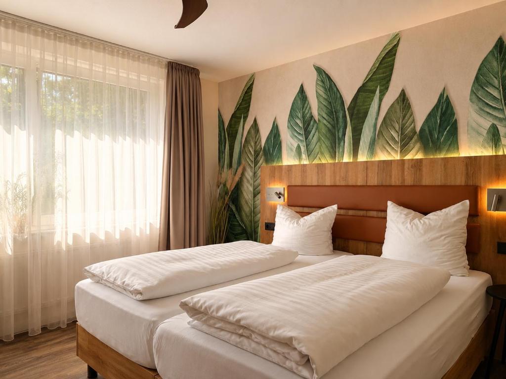 two beds in a bedroom with a mural of leaves at Hotel-Restaurant Amadeus in Hannover