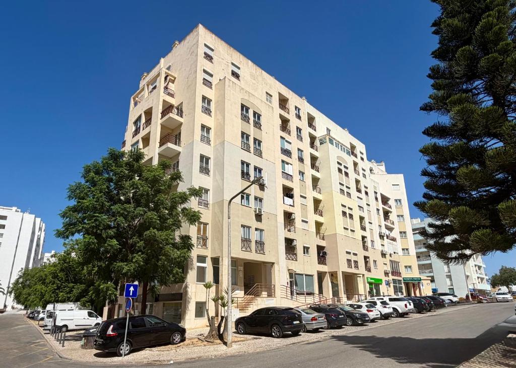 a tall building with cars parked in a parking lot at Rabelo C in Armação de Pêra
