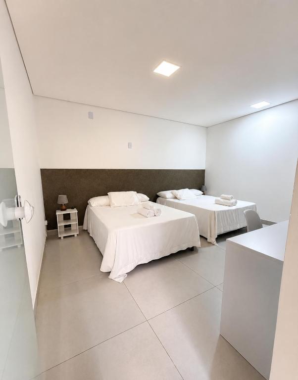 two beds in a room with white walls at Flamboyant Stay Rooms in Goiânia