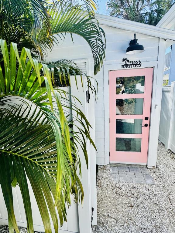 a pink door on a white house with a palm tree at Walk to Siesta Key Beach-Remote Worker Friendly -High Speed WiFi- Bikes Included -Private Fenced In -Close to Restaurants, Coffee Houses & Shops - Paisleys Keep it Simple Casita in Siesta Key