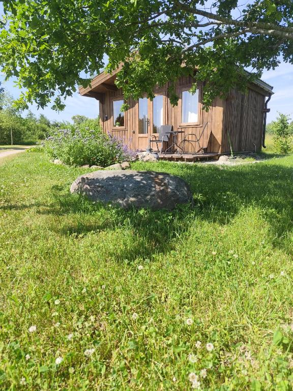 a small cabin with a rock in the grass at Ganu Namiņš in Ķurbes Ciems