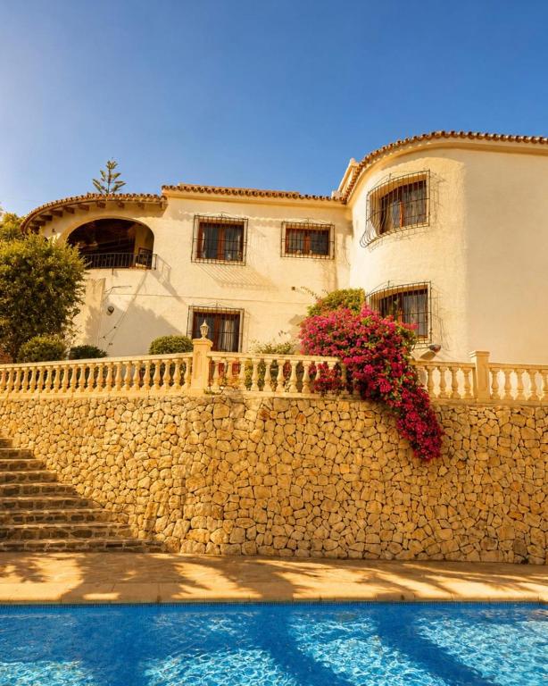 a building behind a stone wall with flowers on it at Casa Toucan Moraira in Benitachell
