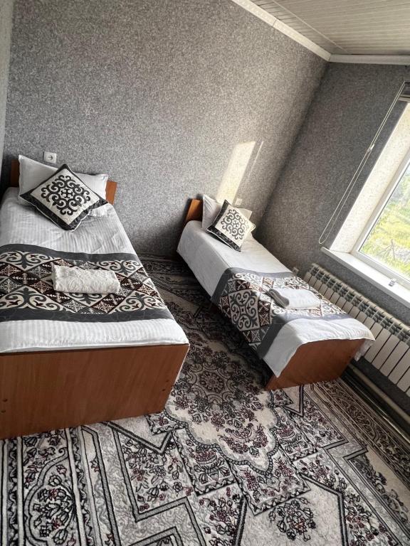 two twin beds in a room with a rug at ERLAN Guest House in Jangy-Talap