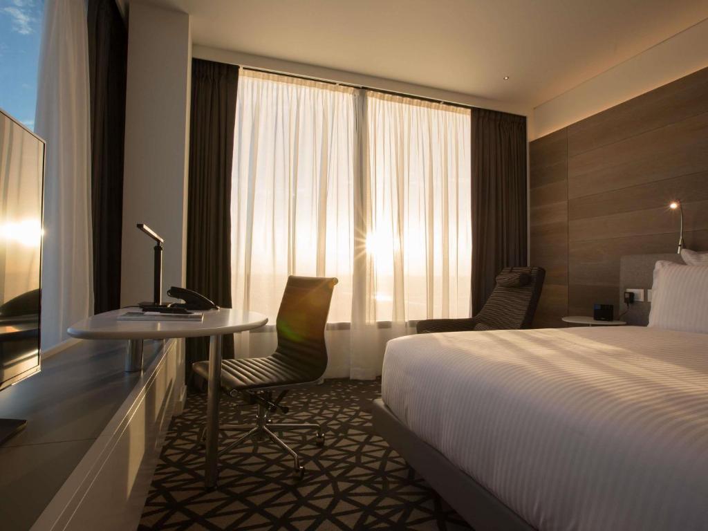 a hotel room with a bed and a desk and a bed and window at Pullman Sydney Airport in Sydney