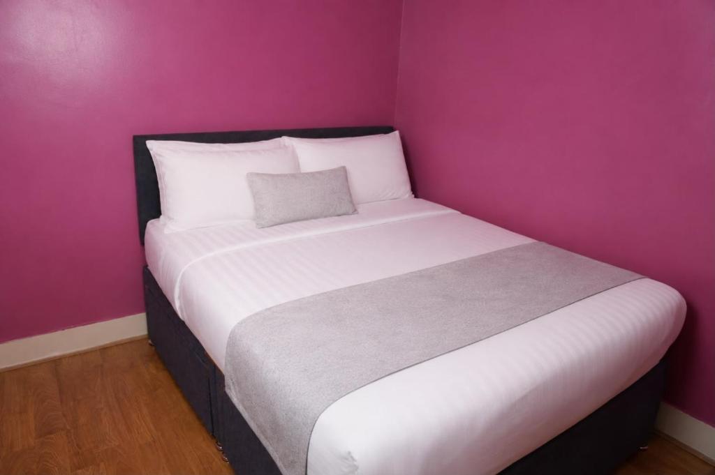 a bedroom with a white bed with a pink wall at Property Reality in London
