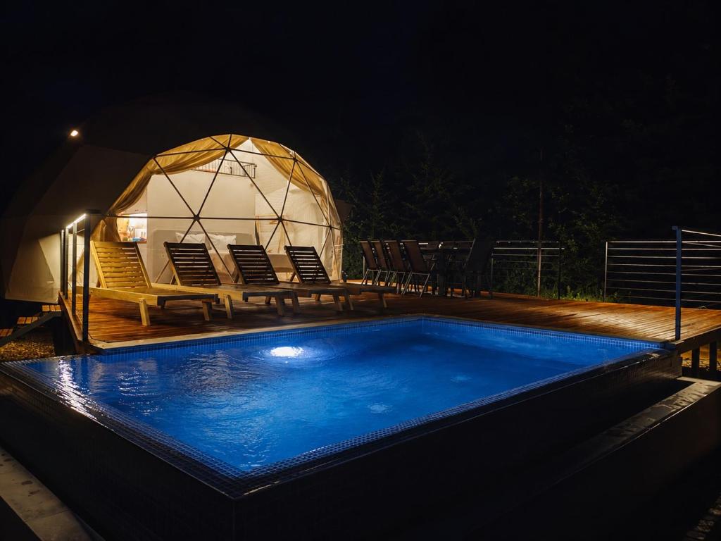 a gazebo with chairs and a swimming pool at night at Kupolica glamping dome in Brčko