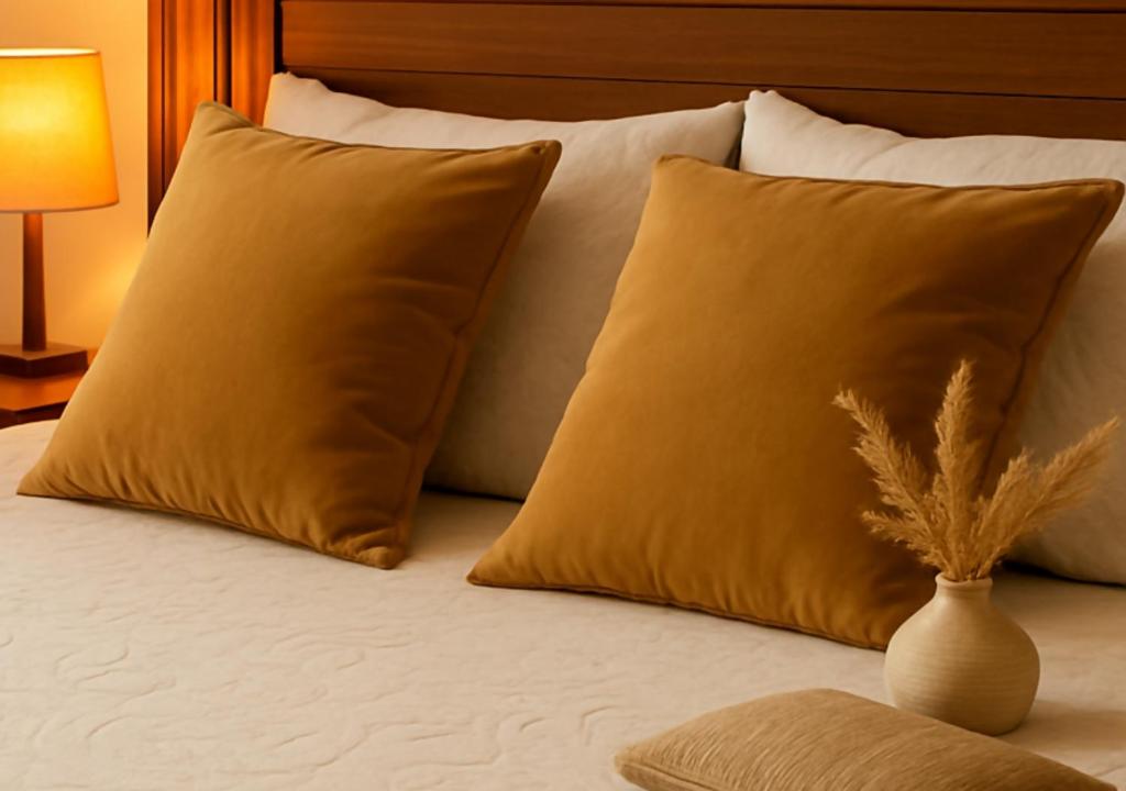 a bed with two pillows and a vase on it at Kariokas Hospedagem in Águeda