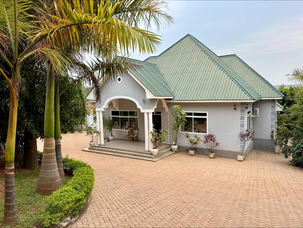 a white house with a green roof and palm trees at COMFORT ZONE Lodge Kigoma in Kigoma