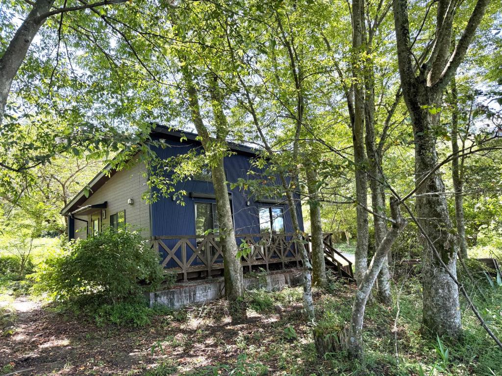 a blue house with a porch in the woods at Starry Forest Inn KURIHAI in Oita