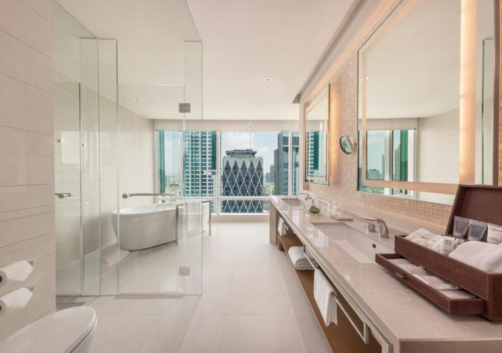 A spacious bathroom with twin sinks, a separate glass shower, and a city view.
