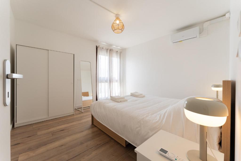 a white bedroom with a bed and a desk with a lamp at A350 Suites - Appartement climatisé, 2 chambres in Colomiers