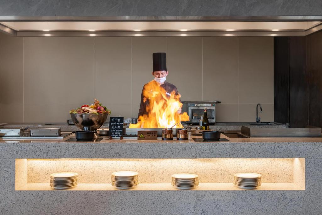 a chef in a top hat cooking over a fire in a kitchen at Kempinski Hotel Xiamen in Xiamen