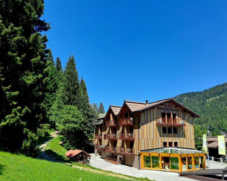 a large building on a hill next to a forest at Hotel Cime D'Oro in Madonna di Campiglio