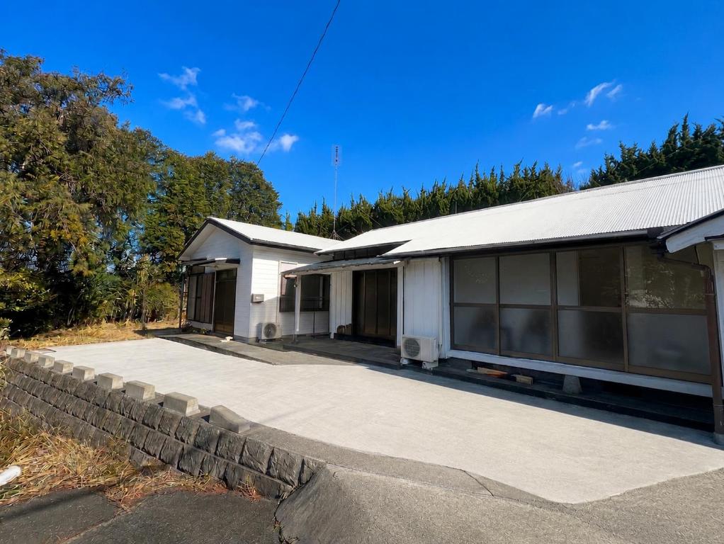 a white house with a stone wall next to a driveway at Guest House TETSU in Oshima