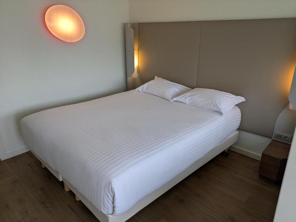 a bed with white sheets and pillows in a room at Hôtel Campanile Orléans Nord - Saran in Saran