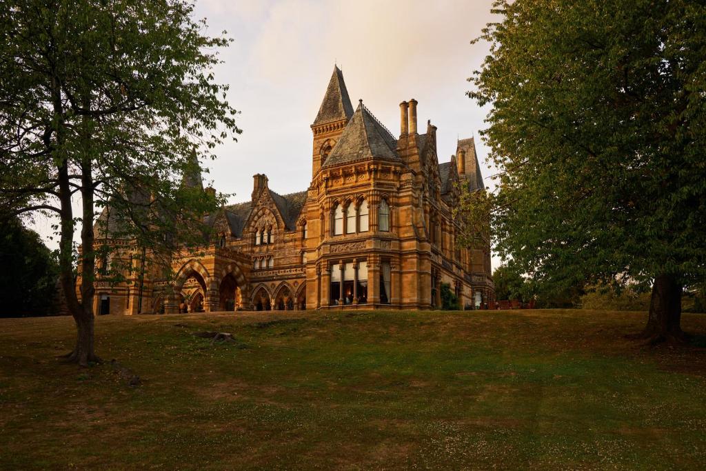an old house on a grassy field with trees at Ettington Park Hotel, Stratford-upon-Avon in Stratford-upon-Avon