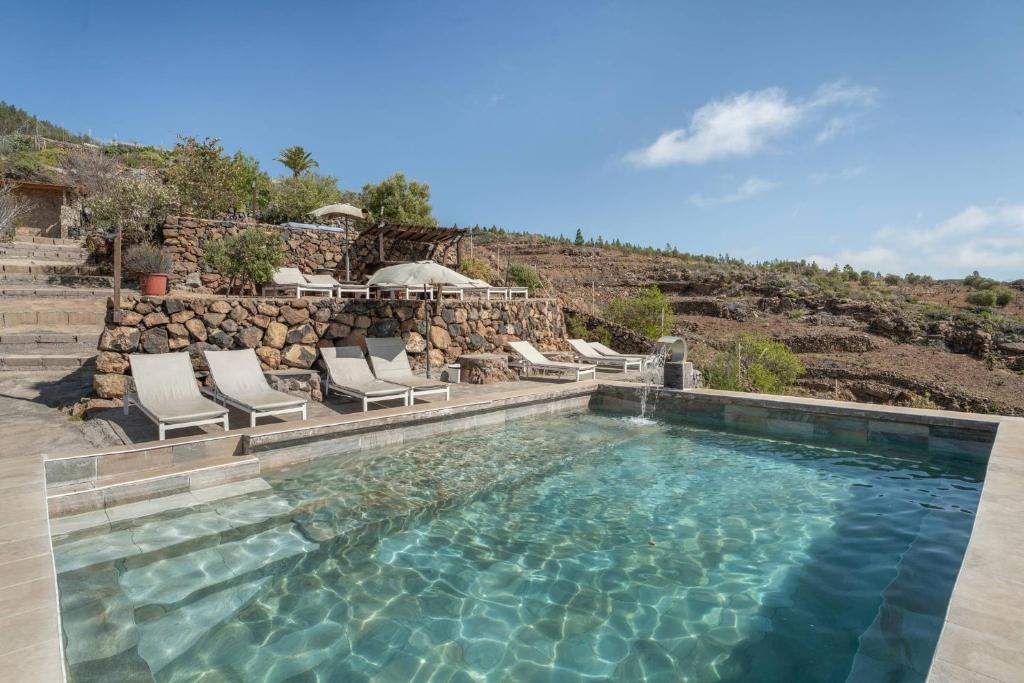a swimming pool with chairs and a rock wall at El cazador 2 in Granadilla de Abona