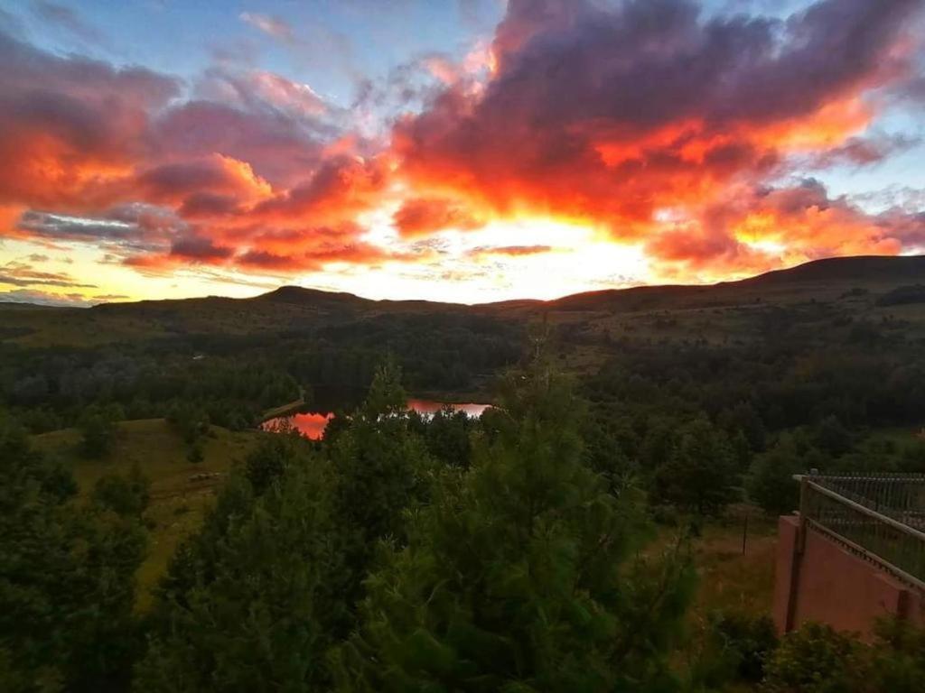 a sunset over a field with trees and mountains at Ukutula Resort in Dullstroom