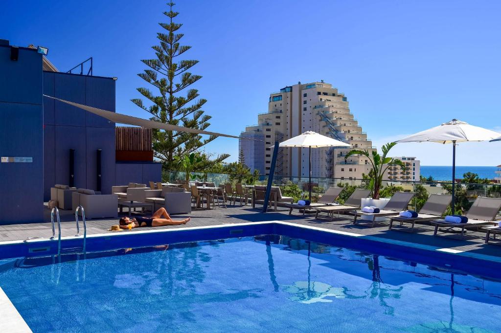 a swimming pool with chairs and umbrellas on a building at The Prime Energize Hotel & SPA - Algarve in Monte Gordo