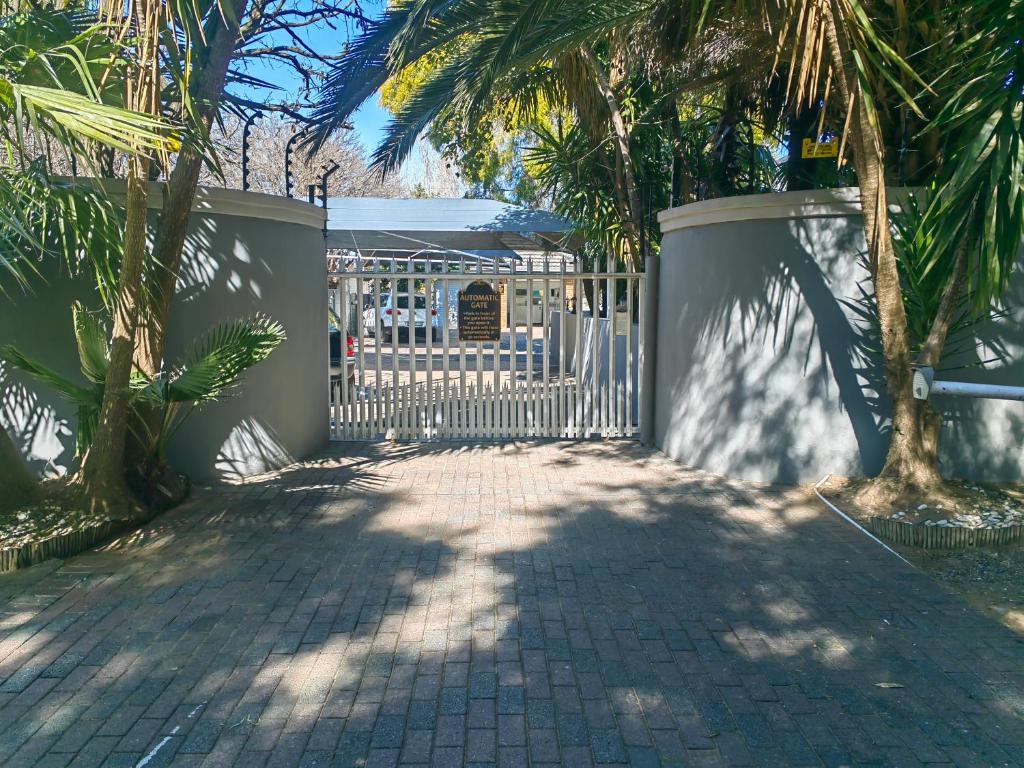 a white gate with a fence and palm trees at Feathers Guest House in Welkom