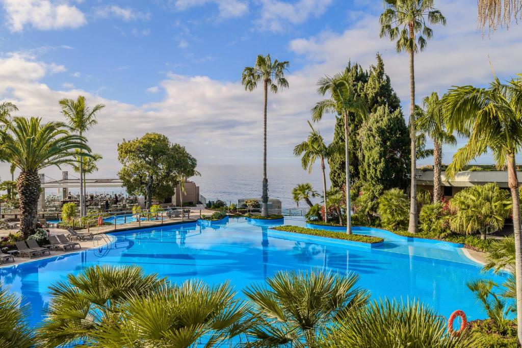 a large pool with palm trees and the ocean at Pestana Carlton Madeira Ocean Resort Hotel in Funchal