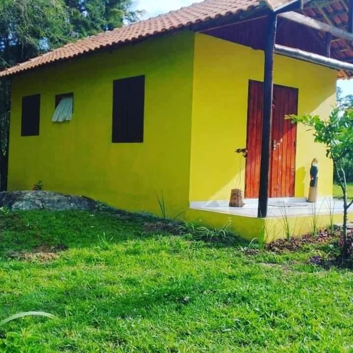 a yellow house with a red door in a yard at Chalé Caminho Real in Itamonte