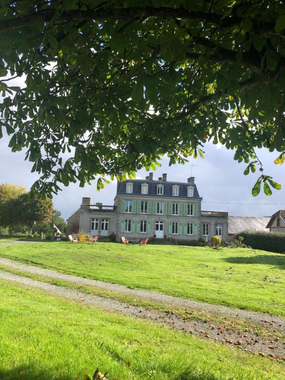a large house on a grassy field with a tree at La Maison du Hommeel in Gratot