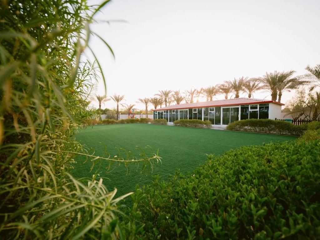 a building with a green lawn in front of it at Palm Escape Farmhouse - By Seven Elements in Ras al Khaimah