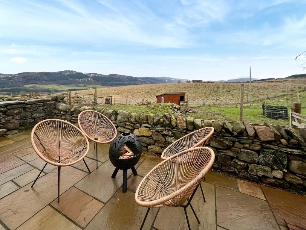 four chairs and a fire pit on a patio with a stone wall at Wellness Cottage At Tomnauld Farm in Pitlochry