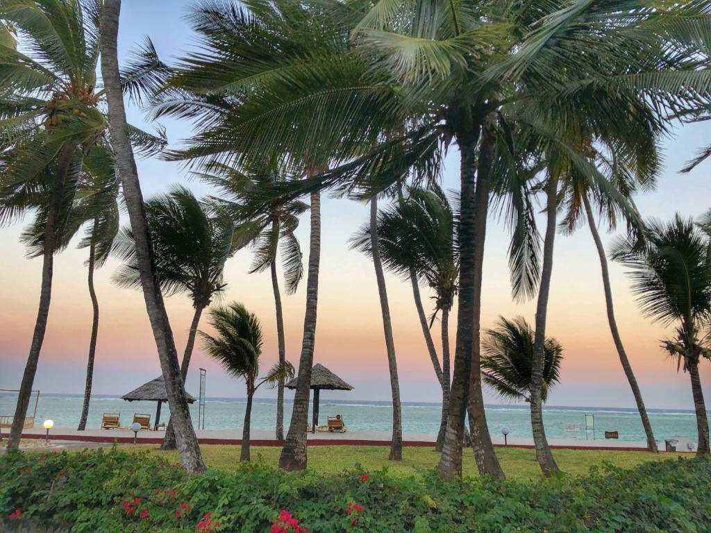 a group of palm trees on the beach at sunset at Diani Reef Beach Resort & Spa - Your Beachfront Bliss Awaits in Diani Beach