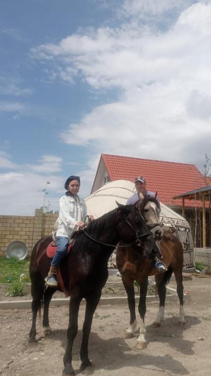two people riding on horses on a dirt road at Ак кайын in Chok-Tal