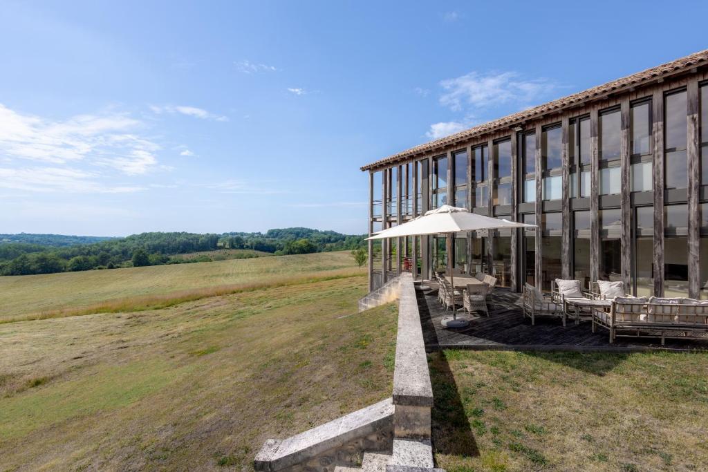 a building with chairs and an umbrella on a field at Maison Lotus - Groupes et familles, séjour Nature au coeur du Périgord Vert in Saint-Martial-de-Valette