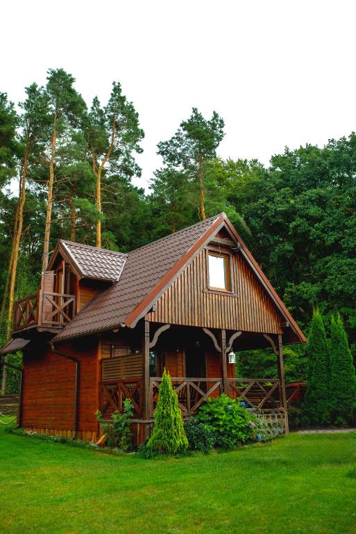 a log cabin with a porch on a green lawn at Domki Pod Lasem Lubkowo in Lubkowo
