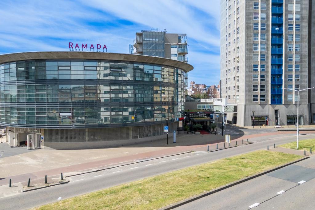 a large glass building in a city with a street at Ramada The Hague Scheveningen in Scheveningen