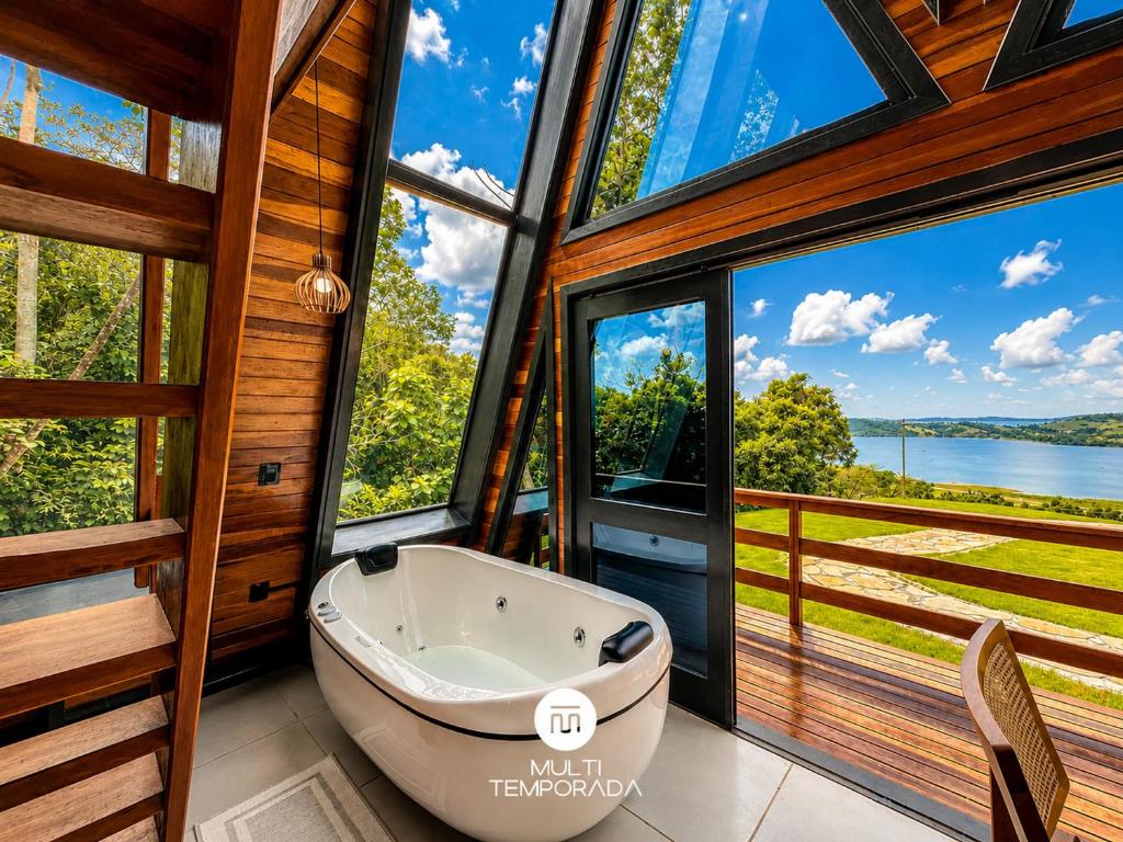 a bathroom with a tub and large windows at Chalés da Lagoa - Imaruí/SC in Imaruí