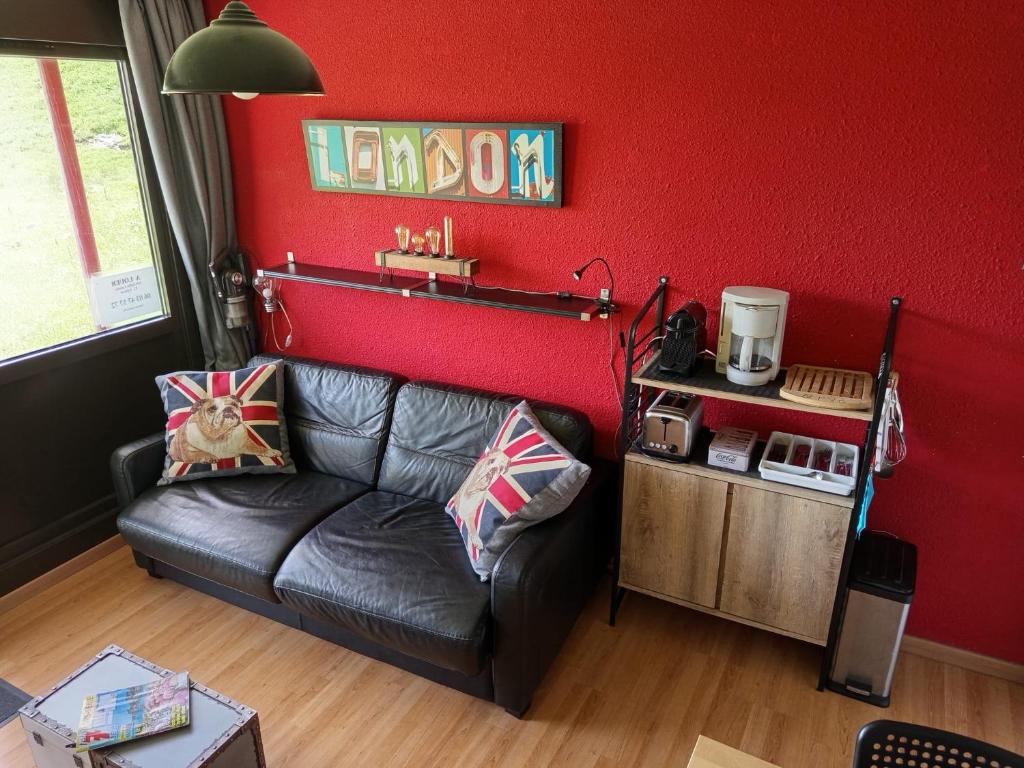 a living room with a black leather couch against a red wall at Studio 4 pers pieds des pistes Piau-engaly in Aragnouet