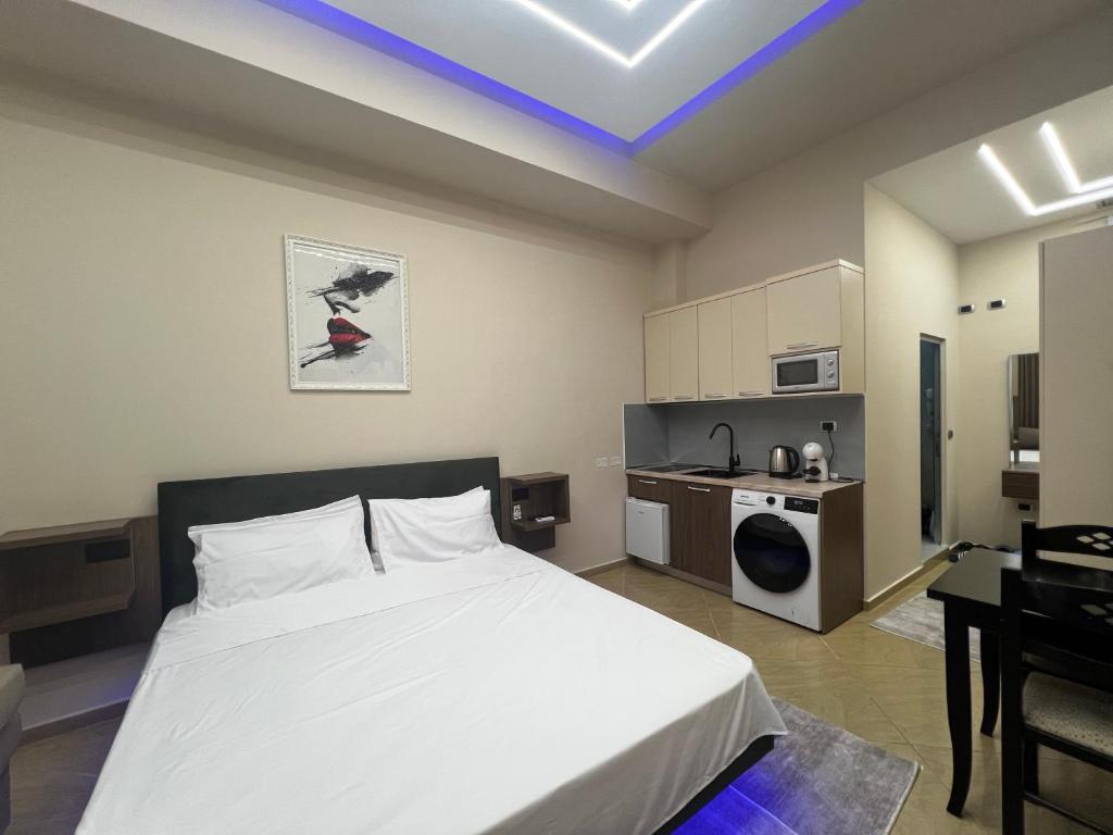 a bedroom with a white bed and a kitchen at Skampa Apartment in Elbasan