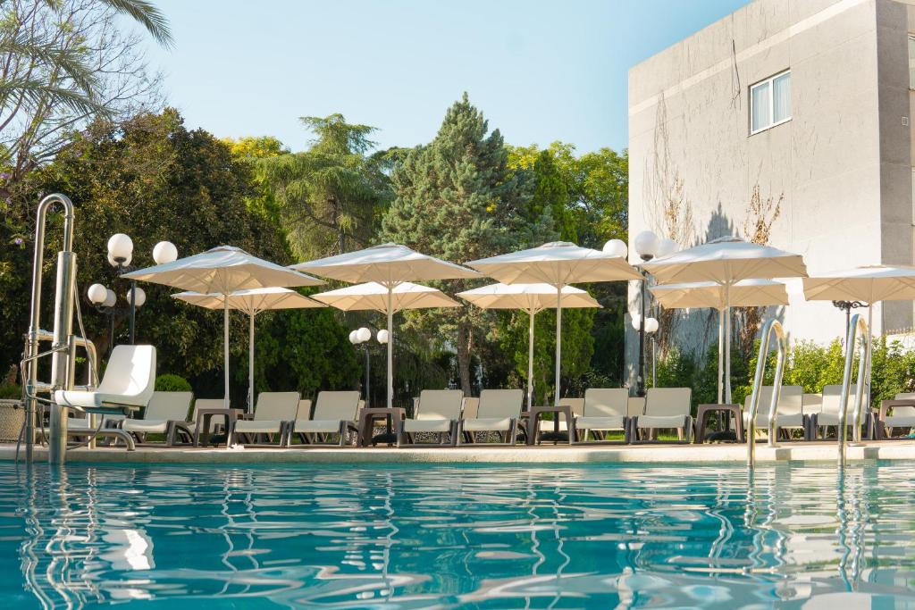 ein Pool mit Liegestühlen und Sonnenschirmen neben einem Gebäude in der Unterkunft Checkin Valencia Ciscar in Picanya