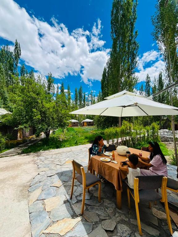 a group of people sitting at a table under an umbrella at Mystique Meadows Swiss Cottages in Nubra