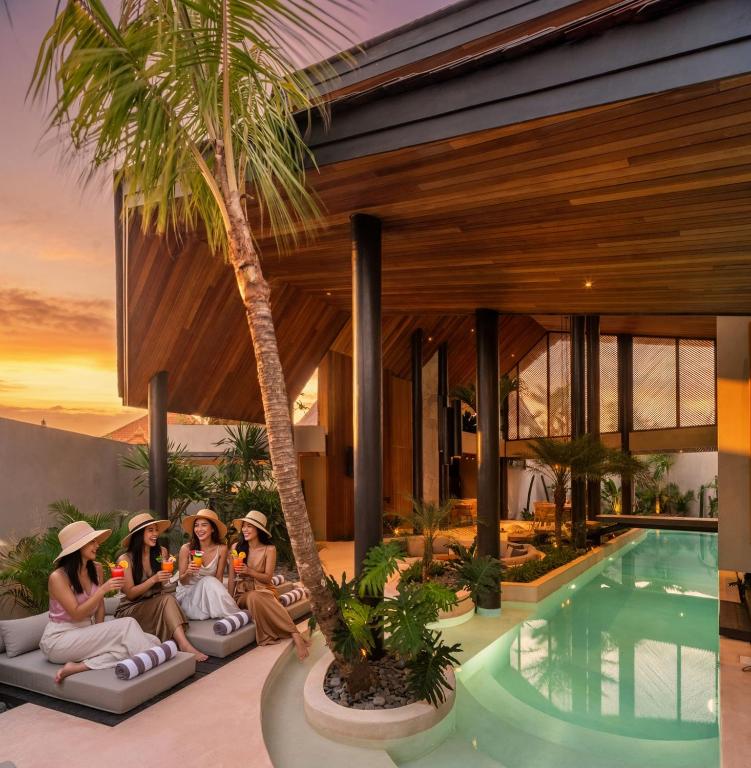 a group of women sitting on a couch next to a swimming pool at Award-Winning 3BR Villa 25m Pool Villa FEH in Kerobokan